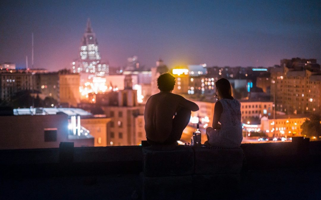 man and woman chilling on rooftop in front of high-rise buildings